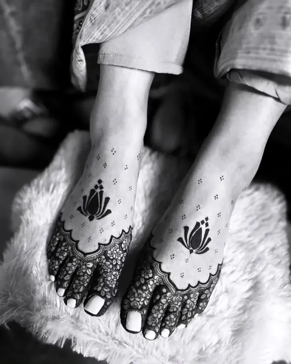An artistic black and white photograph of our lotus foot mehandi. The design features a bold lotus motif on the top of the foot with delicate floral work covering the toes.