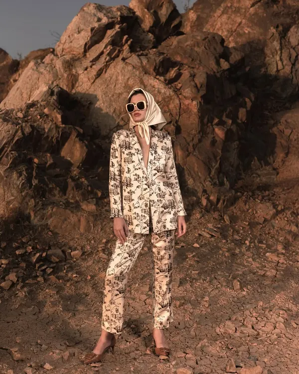 A full-length shot of a modern pantsuit against a rugged, rocky backdrop. This composition contrasts the sharp tailoring of the outfit with the raw texture of the outdoors, creating a striking image for a fashion campaign.