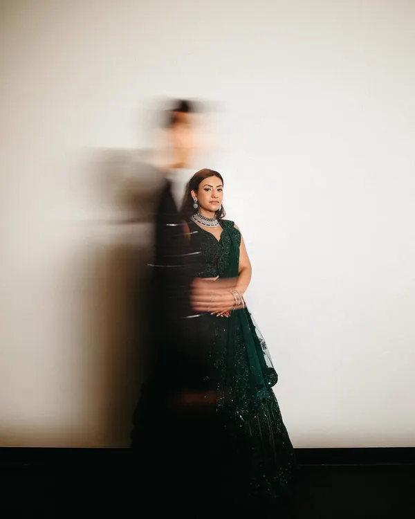 An artistic sangeet portrait using motion blur to create a dynamic and dreamy effect. The bride stands radiant and in focus while the groom is a blur of movement beside her, symbolizing a world that moves fast while their love stands still.