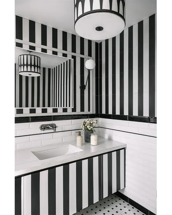 This media lounge powder room at Eden House uses dramatic black and white stripes on the walls and vanity to create a space with immense personality and style. It's where bold drama finds a cozy home.