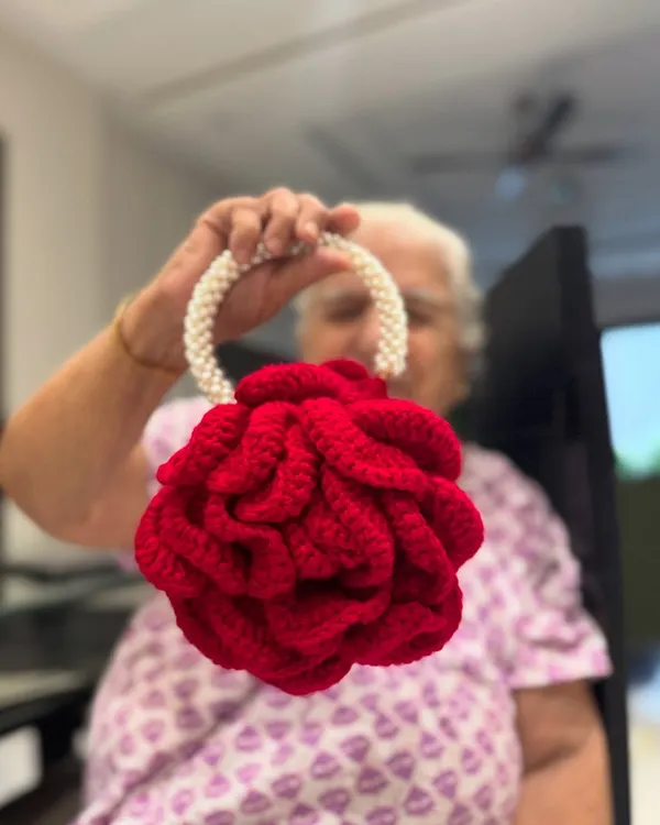 Our signature Peony Bag in a stunning bright red, held by Dadi. This bag is a work of art, featuring a pearl handle and intricate petal-like crochet work.