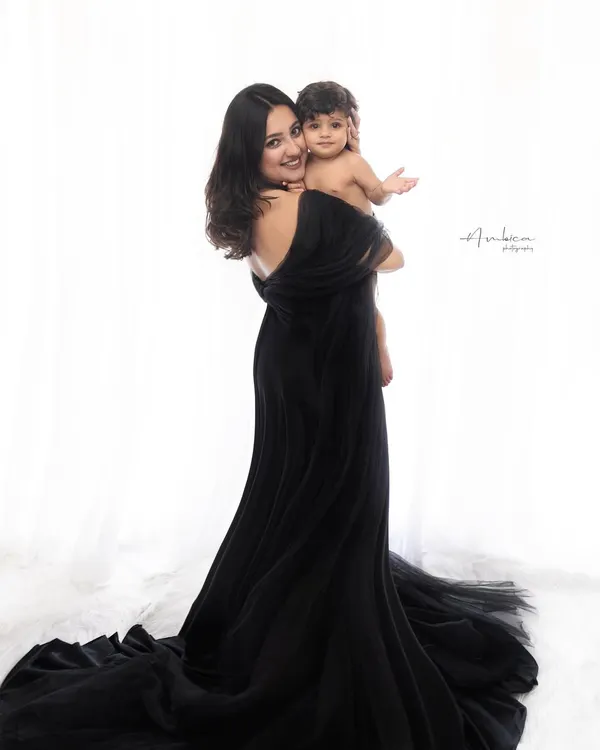 A classic mother and child portrait. The flowing black gown and the simple, high-key background create a look of pure elegance and focus all attention on their connection.