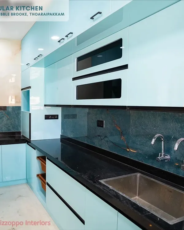 This modular kitchen at Jain's Pebble Brooke features stunning light blue lacquered glass cabinets. The cool tone is beautifully contrasted with a dark green marble-patterned backsplash and a black granite countertop for a sophisticated finish.