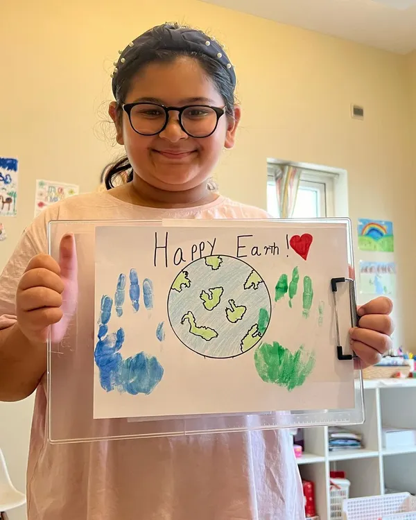 Spreading Earth Day vibes! This young artist is proud of her "Happy Earth" artwork, complete with handprint continents. It's a great way to learn about preserving our beautiful planet.