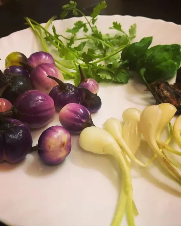 A beautiful plate of the fresh ingredients that form the base of my Naga recipes. You can see the vibrant titaguti, fresh Naga lehsun, coriander, basil, and a piece of ngari (fermented fish).