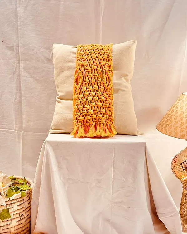 This mustard yellow macrame cushion tie-back features an intricate basket-weave pattern and a fringed bottom. It’s designed to wrap around a plain cushion, instantly transforming it into a decorative statement piece.