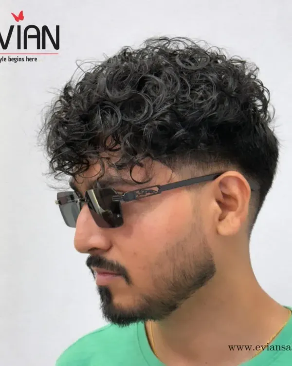 A side profile of this modern curly haircut. The fade is blended perfectly from the temple down, creating a clean and sharp contrast with the textured top.