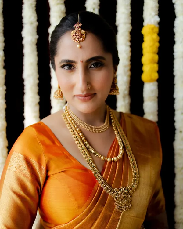 A stunning bridal portrait of a South Indian bride in a traditional orange Kanjivaram saree. Her calm demeanor and elegant jewelry make for a timeless and graceful image.