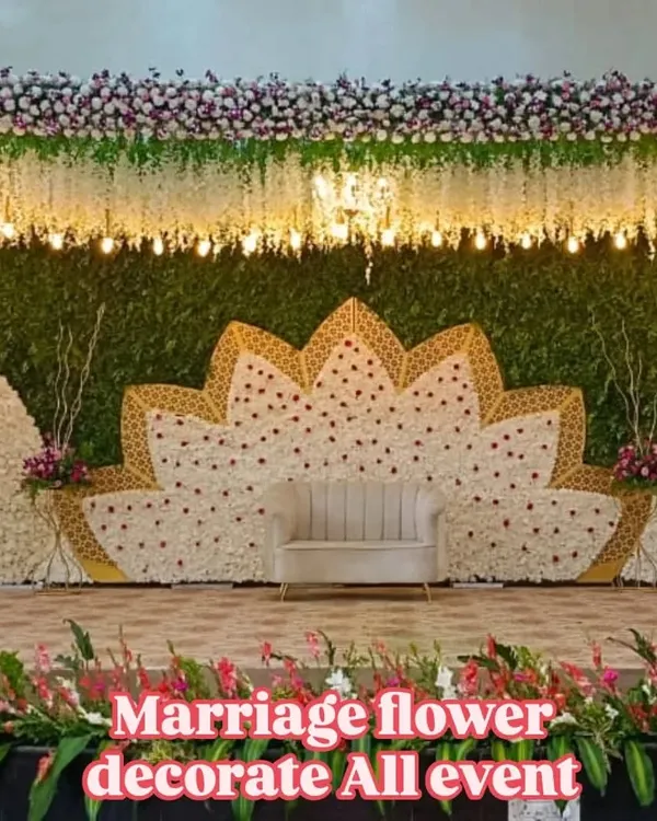A beautiful and modern stage decoration for a wedding reception. The centerpiece is a large, intricate lotus pattern made from white and pink flowers, complemented by a simple, elegant sofa for the couple.