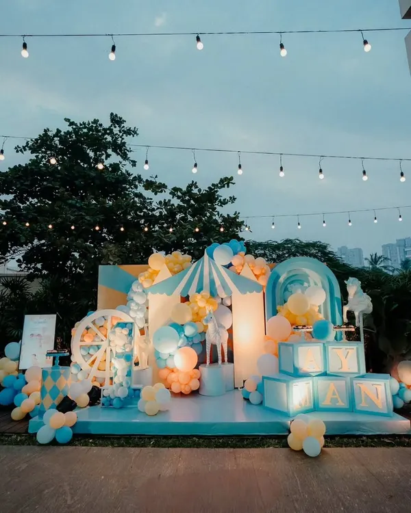 A spectacular carnival theme for a "first birthday" celebration. This outdoor setup features a custom stage, light-up name blocks, a Ferris wheel prop, and a circus tent, all under romantic string lights.