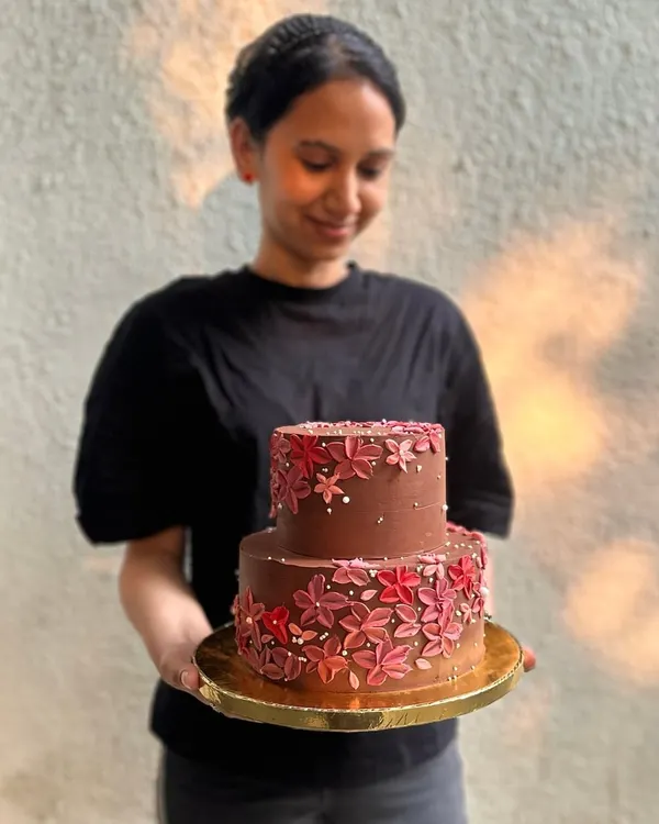 Sanjana from our team holding one of her beautiful creations. This two-tiered chocolate wedding cake is decorated with hand-piped buttercream flowers, a testament to the love and care we put into every order.