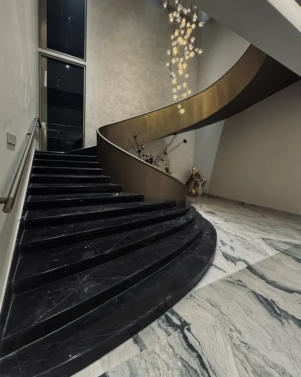 A view of the sculptural staircase from the ground floor. The sweeping curve of the black marble steps and the brass-finished balustrade create a powerful statement of modern elegance.
