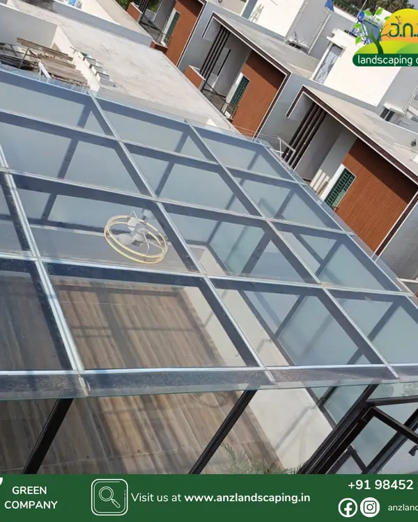 An aerial view of the custom-built glass room for the CEO of IFB Industries Ltd. This shot shows the clear toughened glass roof, which allows for maximum natural light while protecting the interior from the elements.