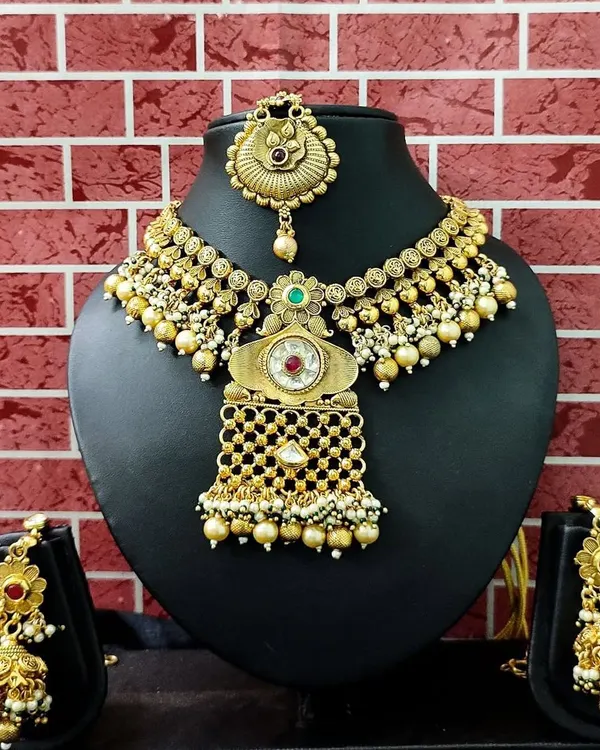 A beautiful antique gold-finish set with a unique design, featuring a choker, matching earrings, and a maang tikka.