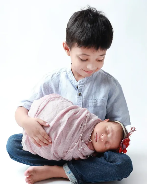 A big brother's gentle protection. He looks down at his sleeping newborn sister with so much love and care.
