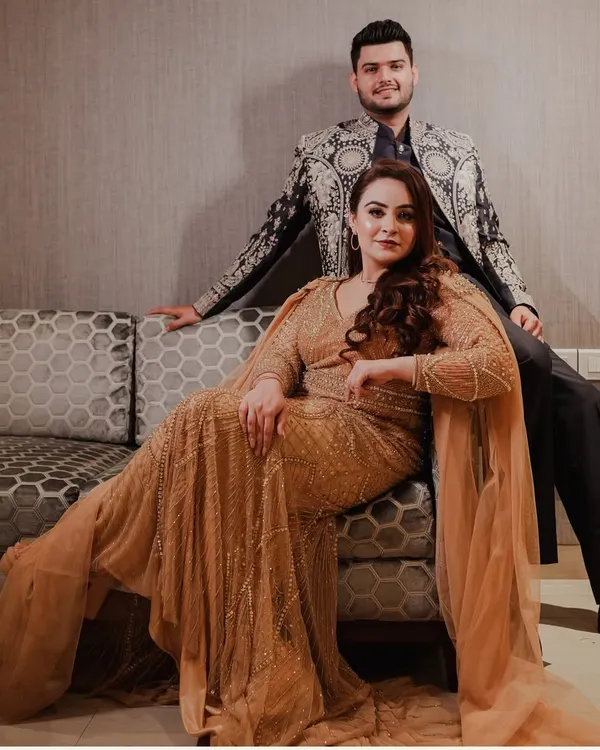 A powerful and glamorous portrait of a couple in stunningly detailed outfits, exuding confidence and elegance in a posed indoor setting.