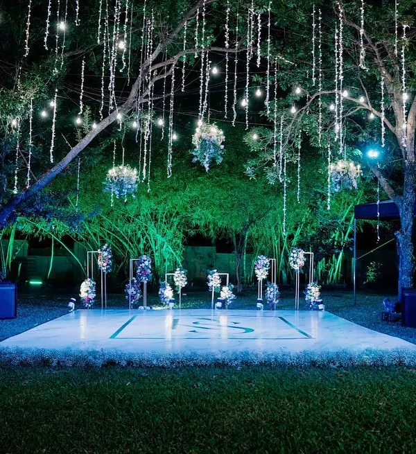 A magical cocktail party setup with a custom dance floor set under a canopy of fairy lights. The hanging floral arrangements and chandeliers add a touch of romance and sophistication to the starry night.