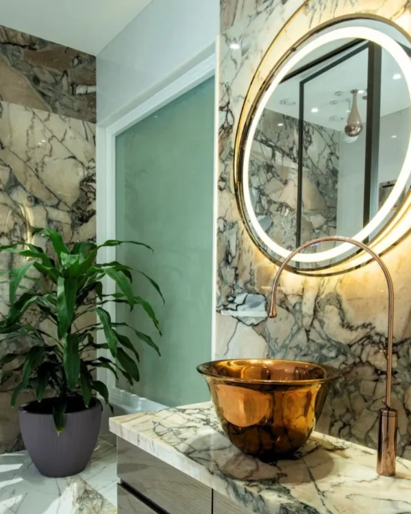 This powder room is designed to make a statement, with floor-to-ceiling dramatic marble, a hammered copper vessel sink, and a backlit mirror. The design composes stone, metal, and light into a functional work of art.