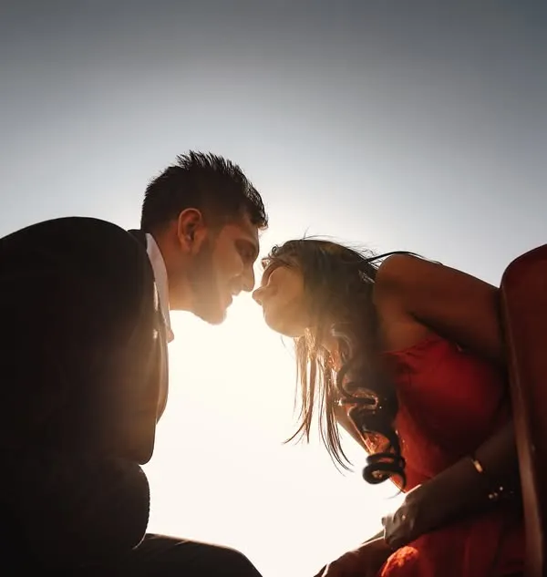 A powerful silhouette of a kiss against the bright sun. This low-angle shot is a creative way to use the golden hour light for a dramatic and artistic pre-wedding photo.
