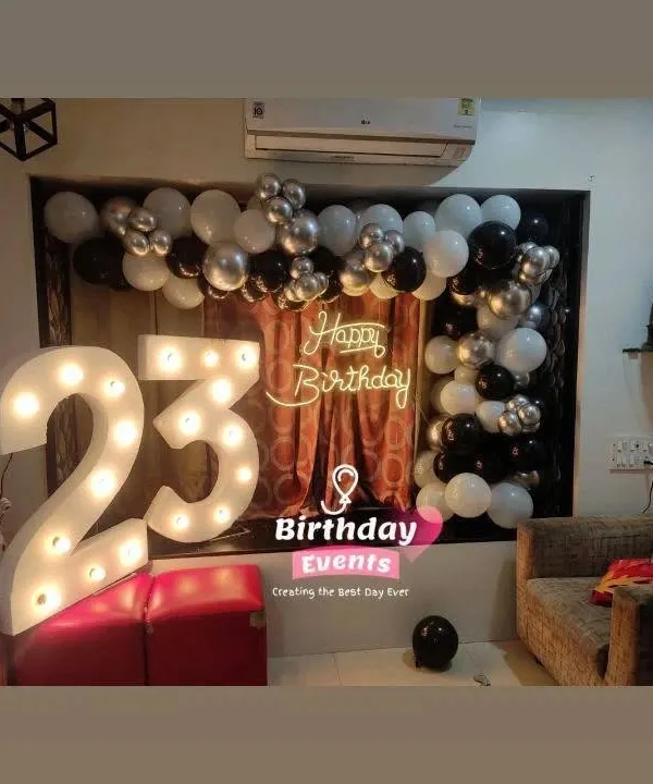 A sleek and modern setup for a 23rd birthday. The large marquee numbers are paired with a simple black, white, and silver balloon arch for a cool, understated look.