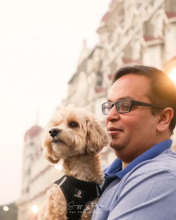A happy portrait of Aaloo the poodle and his dad, sharing a joyful moment in front of the Taj Mahal Palace Hotel in Mumbai.