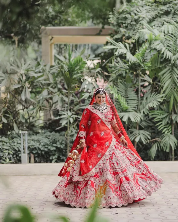 A bride's joy is infectious. We captured this beautiful, uninhibited moment as she twirled in her stunning red lehenga, a perfect blend of traditional elegance and modern happiness set against a lush green backdrop.