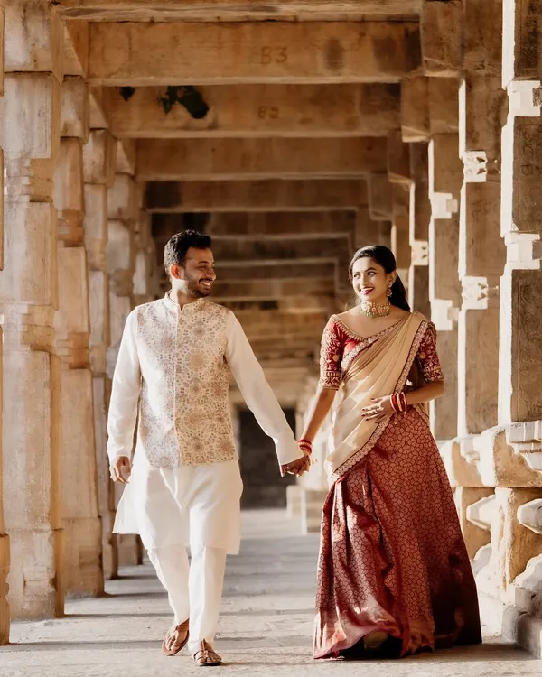 A beautiful couple during their pre-wedding shoot. The bride-to-be is wearing a traditional red and cream brocade half-saree, perfect for creating timeless and romantic memories against a heritage backdrop.