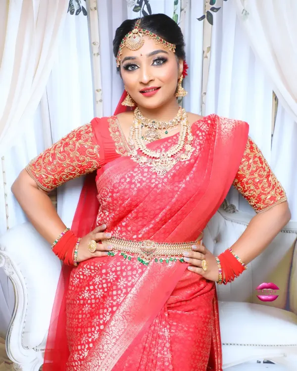 A full-length view of a gorgeous South Indian bridal look. The red Kanjivaram saree is draped perfectly, and the look is completed with a waist belt and traditional gold jewellery.