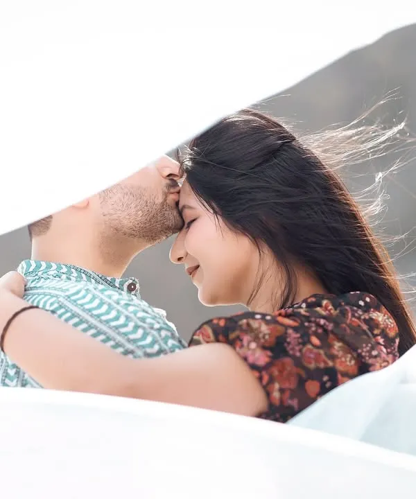 A gentle forehead kiss, with a soft white cloth creating a dreamy, veiled effect. This is a very intimate and artistic portrait.