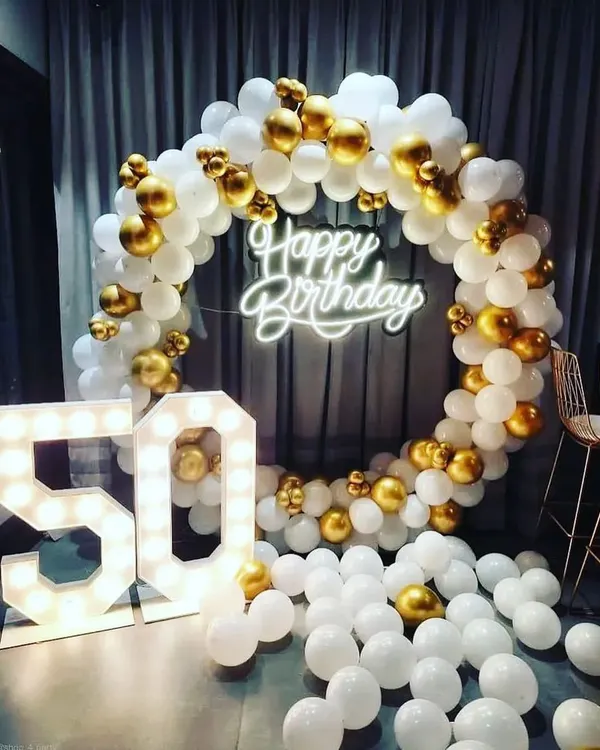 This 50th birthday backdrop features a classic white and gold balloon ring. The large, illuminated marquee '50' stands next to it, creating a glamorous and celebratory photo opportunity for the milestone event.