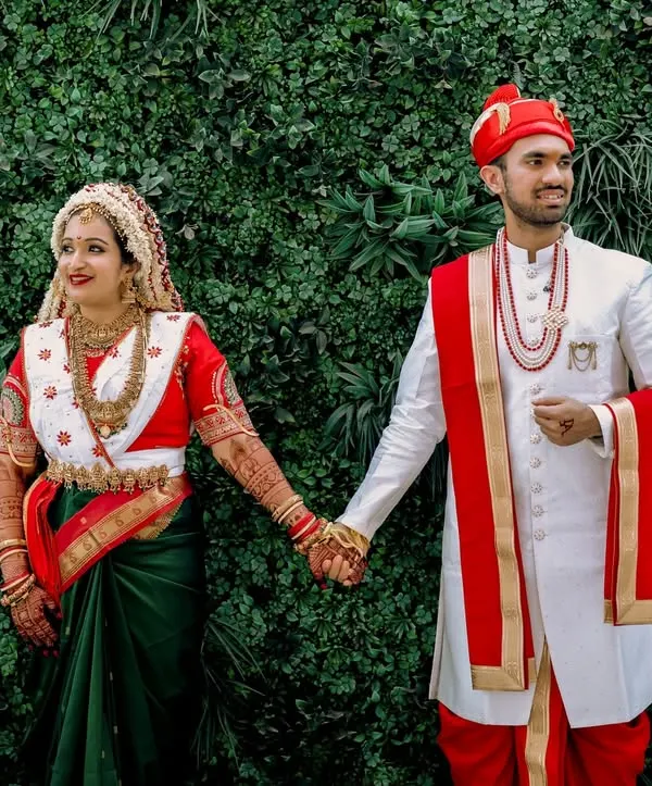 A classic portrait of a Marathi couple, Aditya and Divya. The bride's traditional Nauvari saree and the groom's 'pheta' (turban) are beautifully captured against a lush green backdrop, showcasing the elegance of a Maharashtrian wedding.