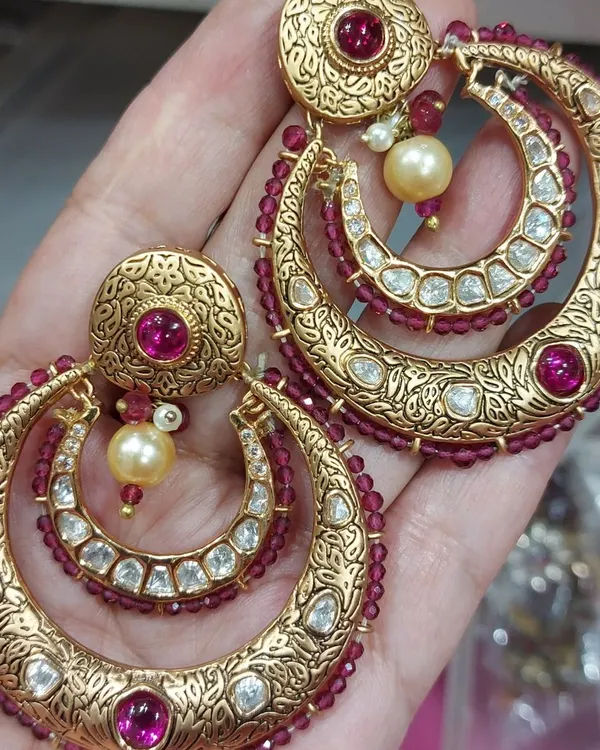 A close-up of our traditional jewellery. These are heavy, gold-plated chandbali earrings with intricate carvings, uncut stones, and ruby-colored beadwork.