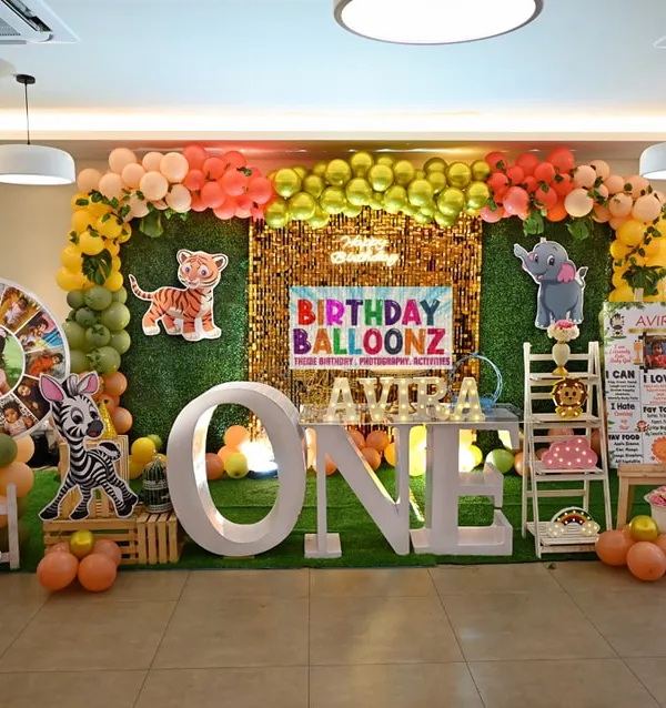 I transform venues into incredible worlds for your child's first birthday. This full jungle safari setup features a lush grass wall backdrop, a custom "ONE" marquee table, character cutouts of a giraffe and zebra, and a vibrant organic balloon garland.