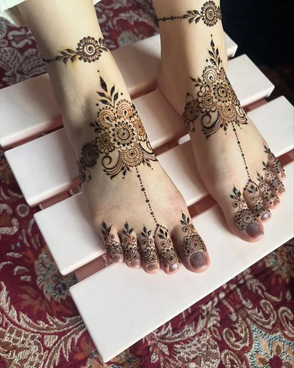 A delicate and modern foot mehendi design. This style features a central motif on the top of the foot with patterns extending to the toes and a matching anklet band.