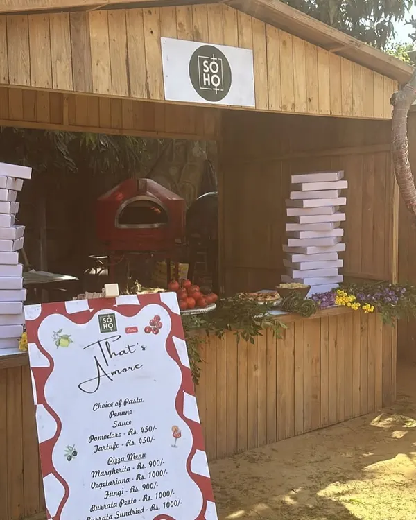 This is my rustic wooden kiosk, set up for an outdoor event. It features my portable red oven, stacks of pizza boxes, and a menu, creating a charming, market-style feel.
