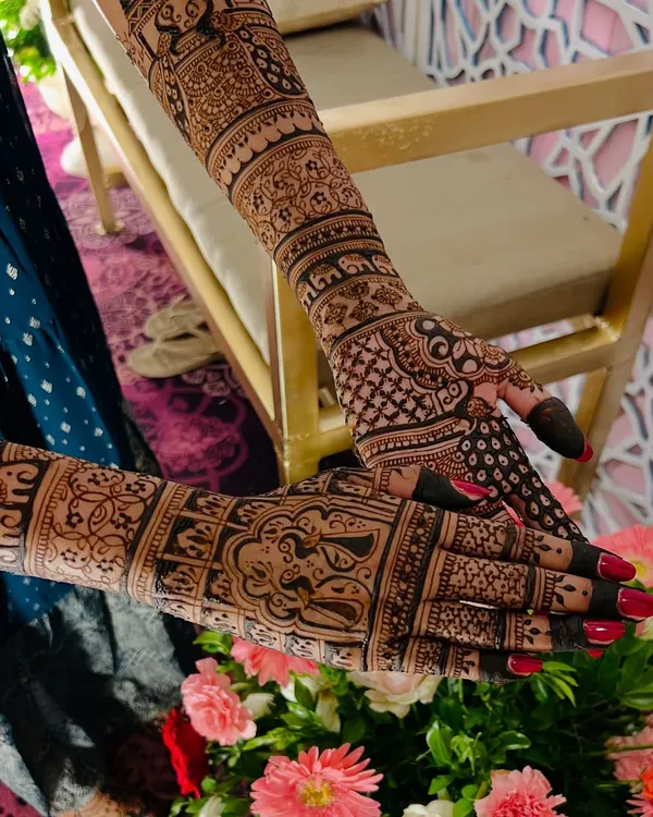 A stunning full-arm bridal design where every detail matters. The composition is set against a beautiful floral backdrop, highlighting the artistry of the henna.