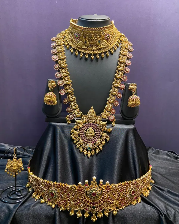 A complete antique bridal set featuring a wide choker, a long haaram with deity pendants, and a matching vaddanam. The intricate design and kemp stones make this a perfect choice for a traditional muhurtham look.