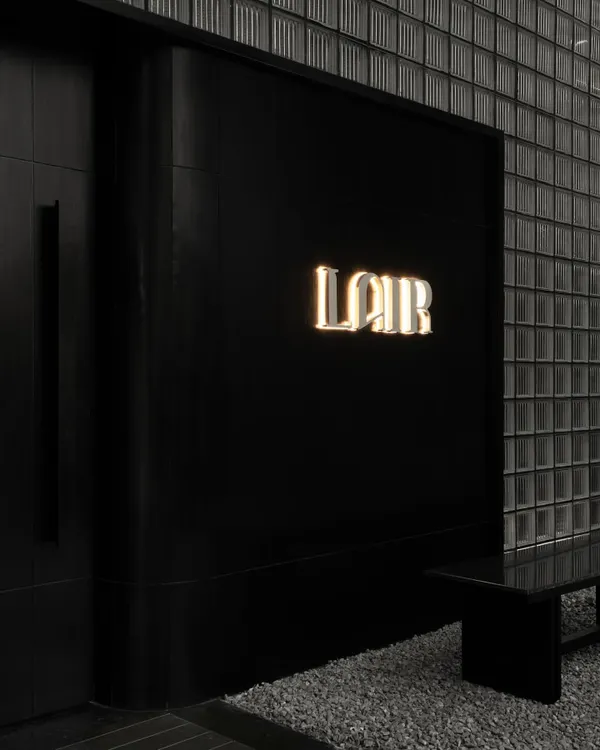 The entrance to Lair, where the brand's name glows against a monolithic black facade and a wall of glass bricks. This is the first clue in a narrative of concealment, hinting at the world that lies behind.