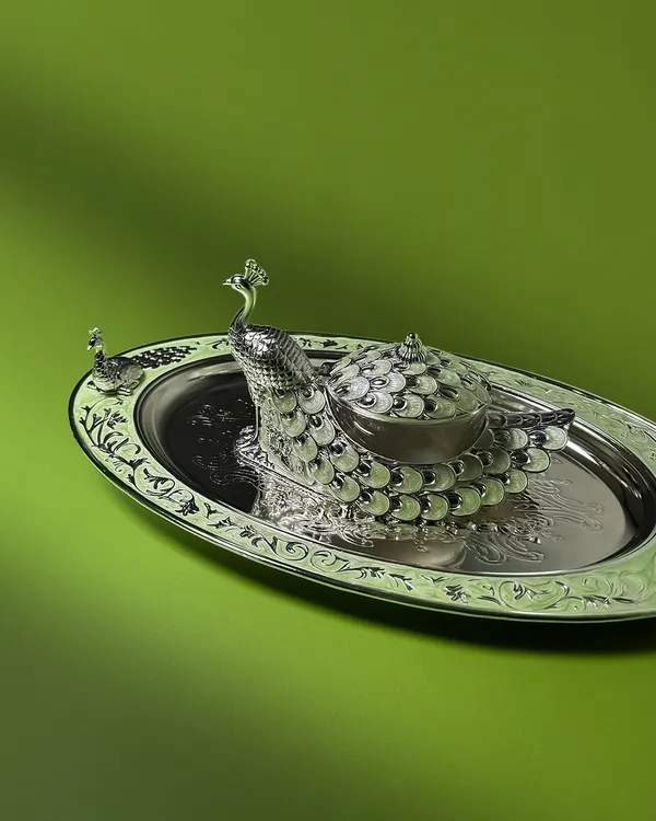 The majesty of the peacock is captured in this stunning silver-plated dry fruit box and tray set. The intricate enamel work and detailed engraving make it a regal centerpiece, perfect for festive hosting or as a luxurious wedding gift.
