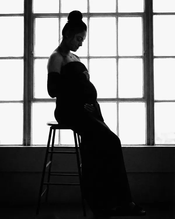 A powerful black and white silhouette of the mother-to-be. Seated on a stool against a window, this artistic shot uses shadow and light to create a moody and contemplative portrait.