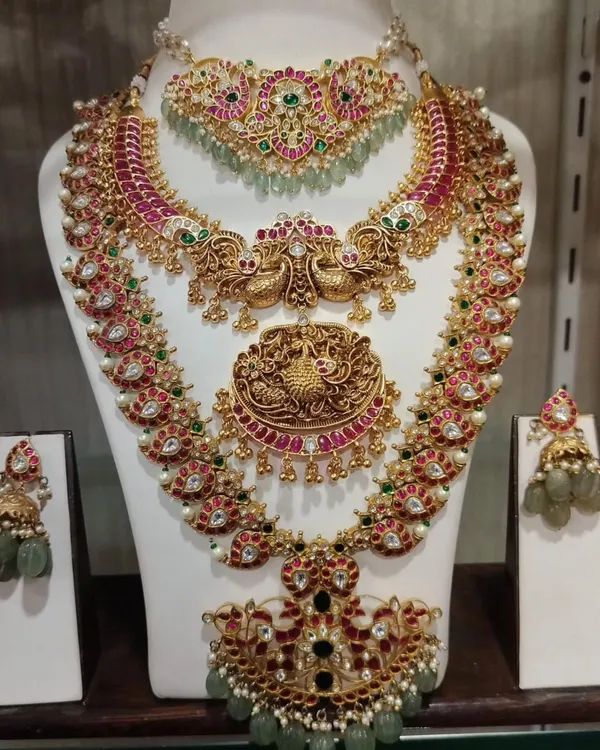 A grand Kempu bridal set with a mix of ruby, emerald, and uncut stones. This layered set includes a choker, a peacock-motif haram, and a statement pendant necklace.