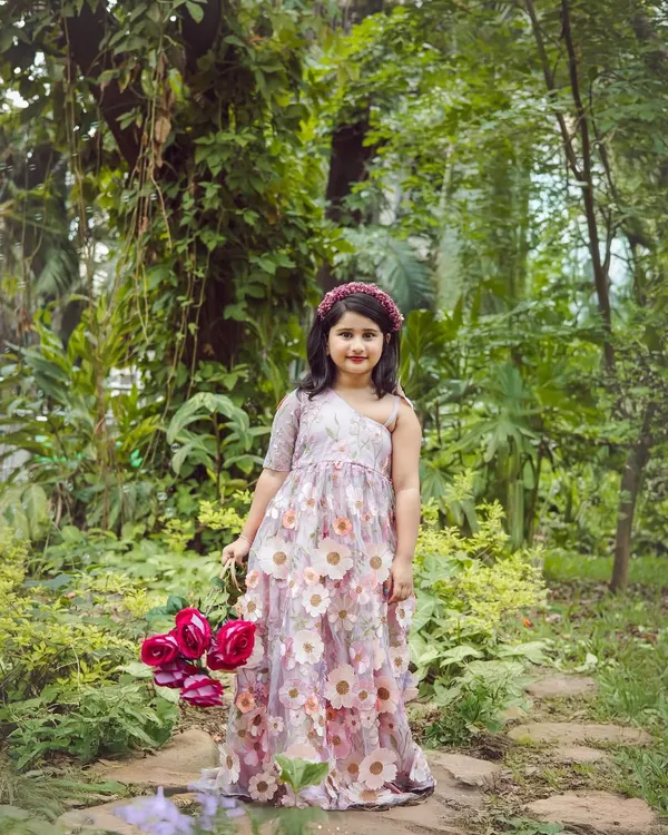 A whimsical outdoor portrait of a little girl in a beautiful floral dress, holding a basket of roses. The lush green background makes her feel like a character from a fairy tale.