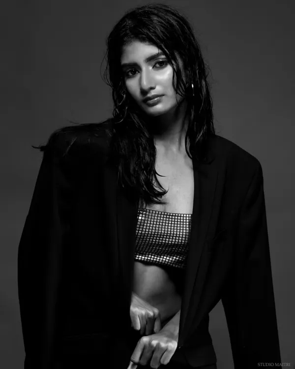 A dramatic black and white portrait of a model with the "wet look," wearing a silver top and black blazer. The high-contrast lighting creates a powerful, editorial feel.