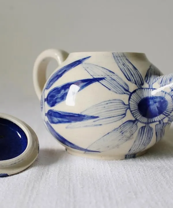The 'Bloom & Brew' teapot with its lid off, showing the deep indigo glaze inside. Every part of the piece is handcrafted, from the body to the spout and handle.