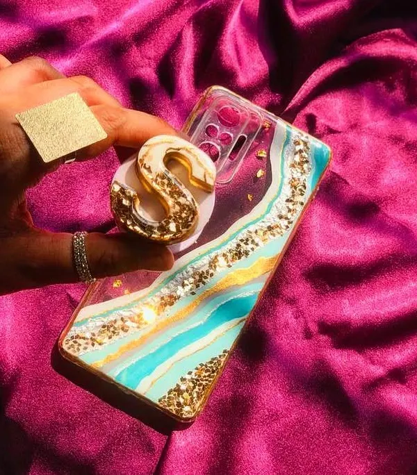 This geode-style phone case features turquoise and white resin with gold accents, paired with a matching initial pop socket. It's a glamorous and personalized accessory.