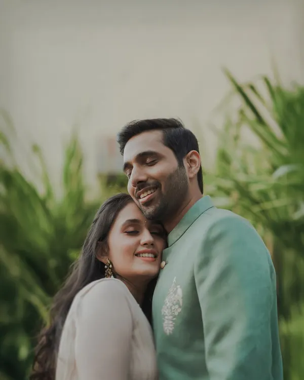 A heartfelt portrait of a couple embracing, their eyes closed in a moment of pure comfort and happiness. The lush green background adds to the natural, candid feel of this engagement photo.