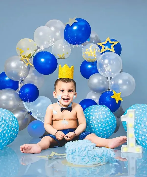A classic cake smash for a first birthday! This little prince is having the best time with his blue-themed setup, complete with a crown and a delicious cake.