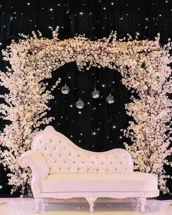 This engagement ceremony photobooth features a stunning arch of white cherry blossoms against a starry black backdrop. The elegant chaise lounge provides the perfect spot for beautiful, timeless photos.