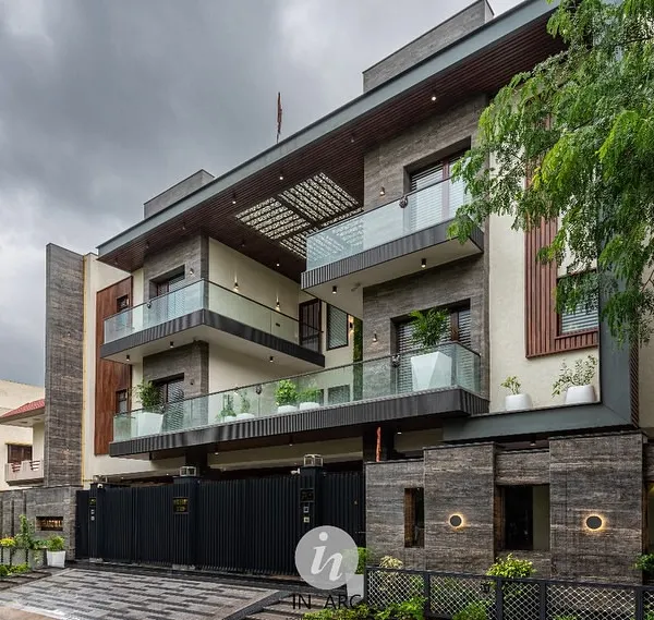 Another view of the completed residence in Greater Noida. The design uses a mix of stone cladding and wood-finished louvers to create texture and visual interest across multiple levels.
