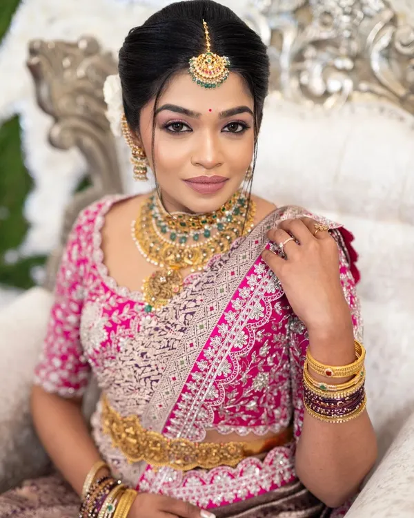A close-up of our beautiful bride, radiant in her custom-designed pink Benarasi silk saree blouse. The intricate zardozi and pearl work on the blouse, paired with a traditional vaddanam, creates a timeless and elegant bridal look.